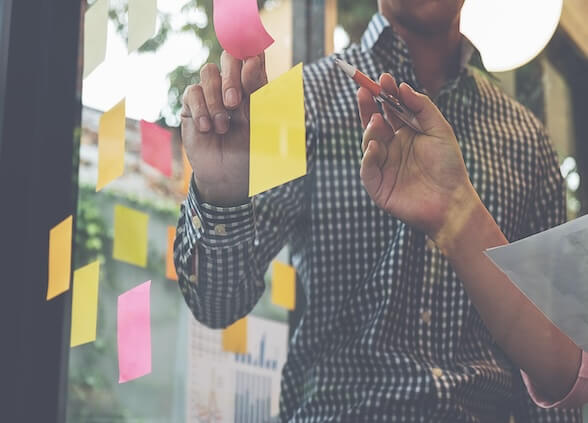 People writing on sticky notes on a glass board